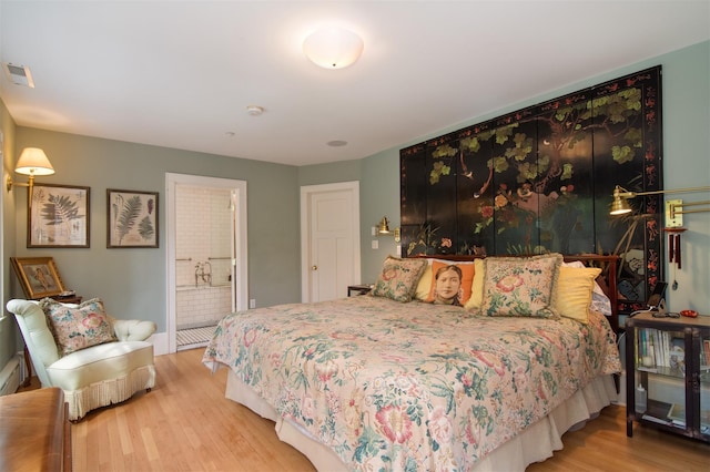 bedroom with baseboards, connected bathroom, wood finished floors, and visible vents