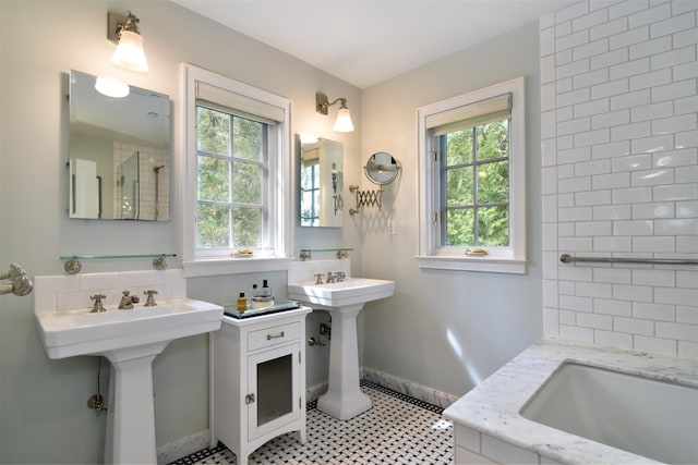 bathroom featuring baseboards, walk in shower, a bath, and two sinks