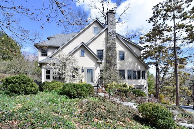 view of front of house featuring a chimney, a shingled roof, and stucco siding