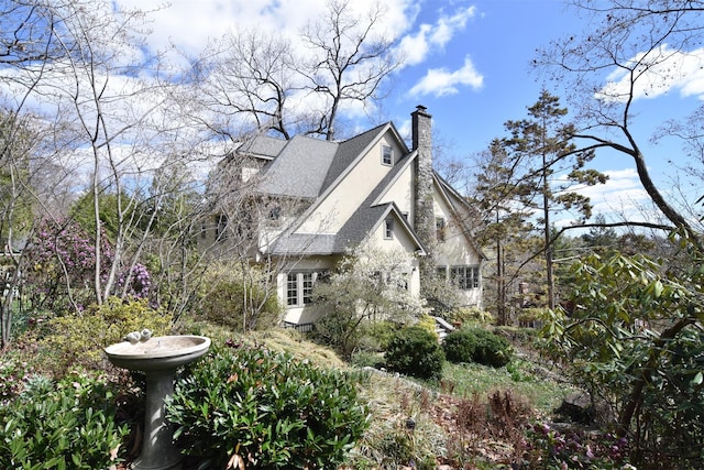 view of side of home with roof with shingles, stucco siding, and a chimney