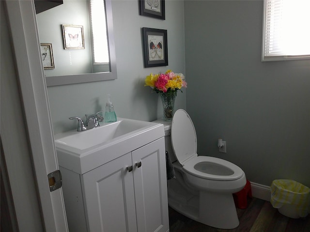 half bathroom featuring vanity, baseboards, toilet, and wood finished floors
