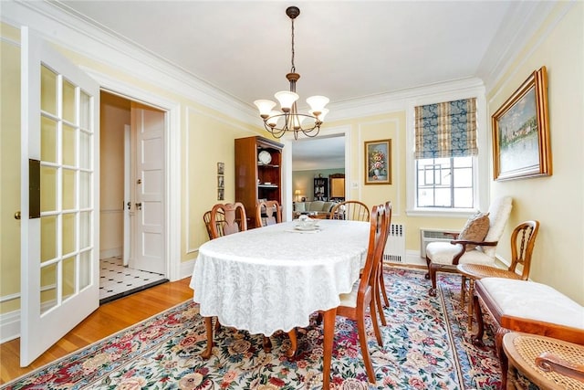 dining area featuring an inviting chandelier, radiator, ornamental molding, and wood finished floors