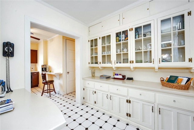 interior space featuring light countertops, white cabinets, glass insert cabinets, light floors, and ornamental molding