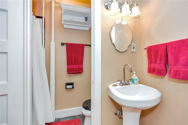 full bath with a sink, tile patterned floors, baseboards, toilet, and a notable chandelier