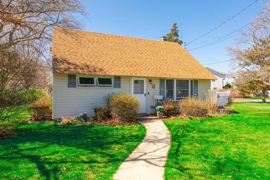 cape cod house featuring a front yard, a chimney, and roof with shingles