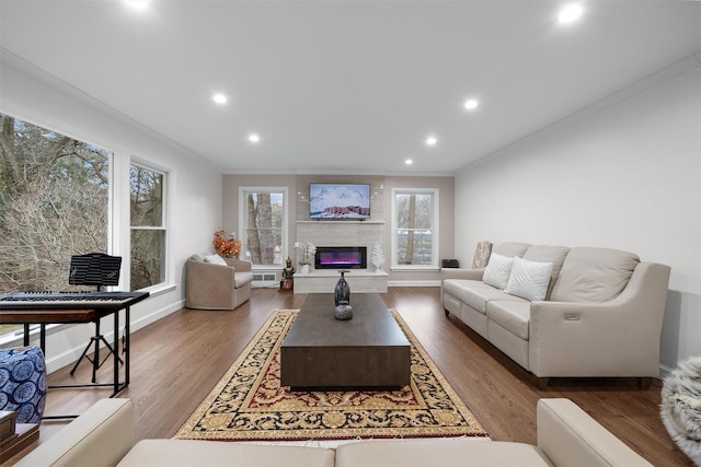 living area with recessed lighting, a glass covered fireplace, wood finished floors, and crown molding