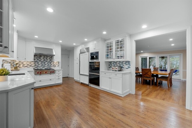 kitchen featuring wall chimney exhaust hood, white cabinets, a sink, light wood-type flooring, and decorative backsplash