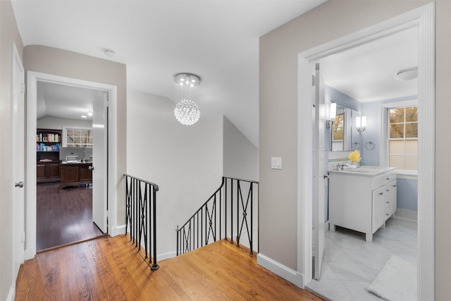 hall with baseboards, wood finished floors, and an upstairs landing