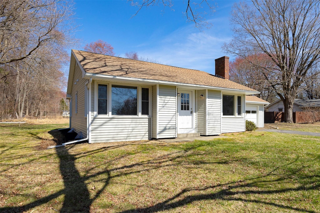 view of front of home featuring a shingled roof, entry steps, a garage, a chimney, and a front lawn