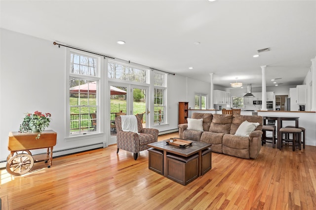 living area featuring a baseboard heating unit, light wood-style flooring, baseboard heating, and decorative columns
