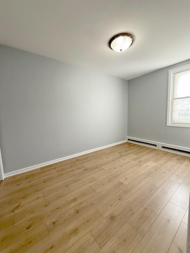 empty room featuring light wood-style flooring, a baseboard radiator, and baseboards