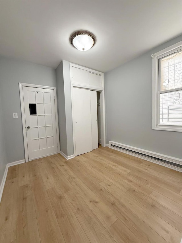unfurnished bedroom featuring a baseboard radiator, a closet, baseboards, and light wood-type flooring