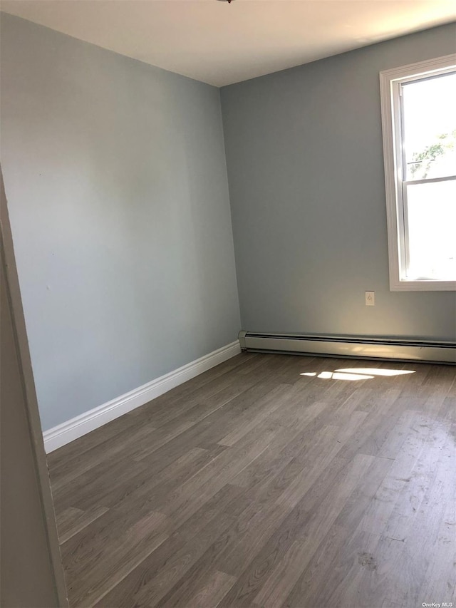 empty room featuring dark wood-type flooring, a baseboard heating unit, and baseboards