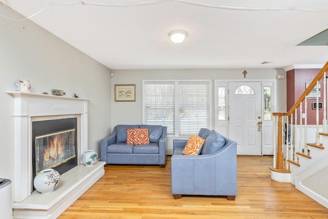 living area with a glass covered fireplace, light wood-style flooring, and stairs