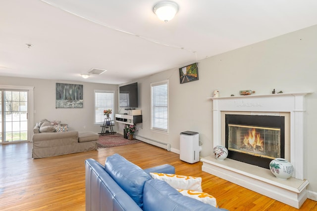 living area with a baseboard heating unit, wood finished floors, and visible vents