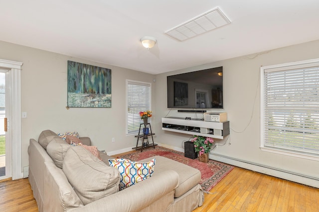 living area with baseboard heating, visible vents, hardwood / wood-style flooring, and a healthy amount of sunlight