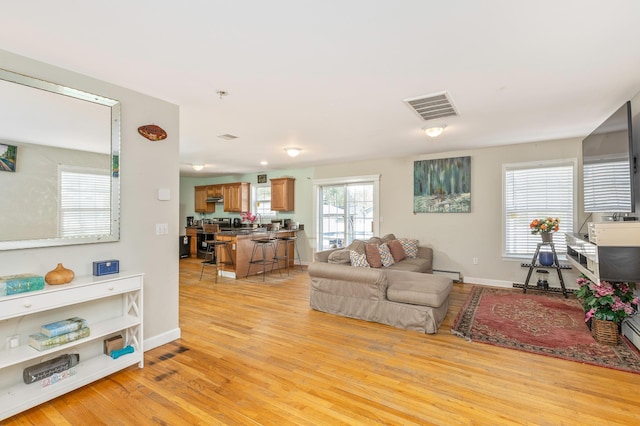 living room featuring baseboard heating, baseboards, visible vents, and light wood-type flooring