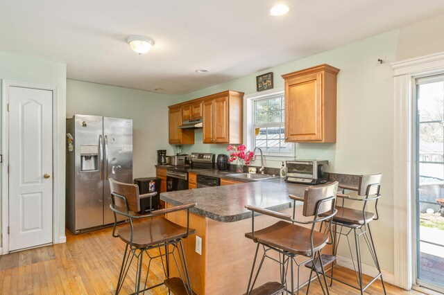 kitchen featuring under cabinet range hood, dark countertops, a sink, a peninsula, and appliances with stainless steel finishes