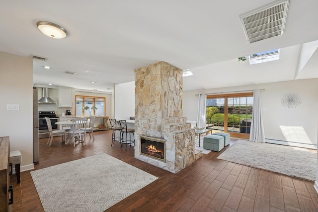 living area with dark wood-style flooring, visible vents, a stone fireplace, and baseboard heating