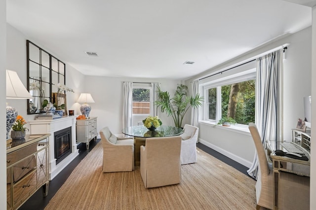 dining space with a glass covered fireplace, wood finished floors, visible vents, and baseboards