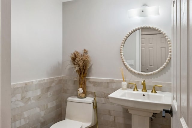half bathroom featuring wainscoting, toilet, a sink, and tile walls