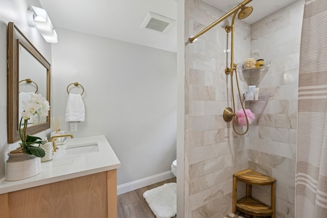 full bathroom featuring wood finished floors, visible vents, toilet, vanity, and tiled shower
