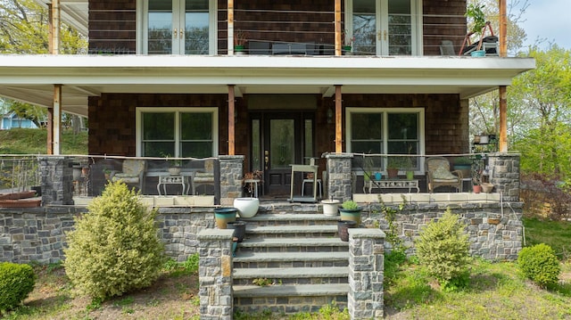 view of exterior entry with a porch, a balcony, and french doors