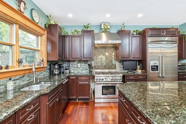 kitchen with a sink, backsplash, wall chimney range hood, and high quality appliances