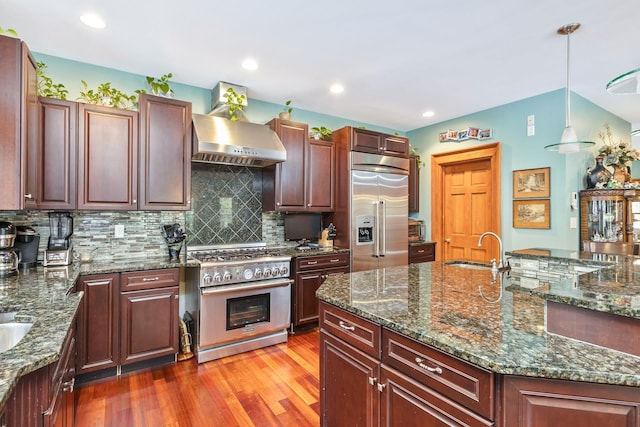 kitchen with hanging light fixtures, a sink, light wood-style flooring, high end appliances, and backsplash
