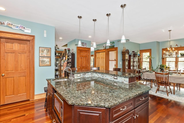 kitchen with a sink, a notable chandelier, dark wood-style floors, and a center island with sink