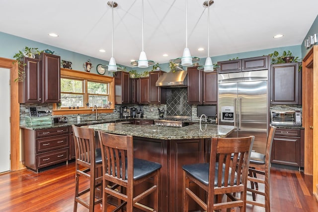 kitchen featuring stainless steel built in fridge, decorative backsplash, a sink, and wall chimney exhaust hood