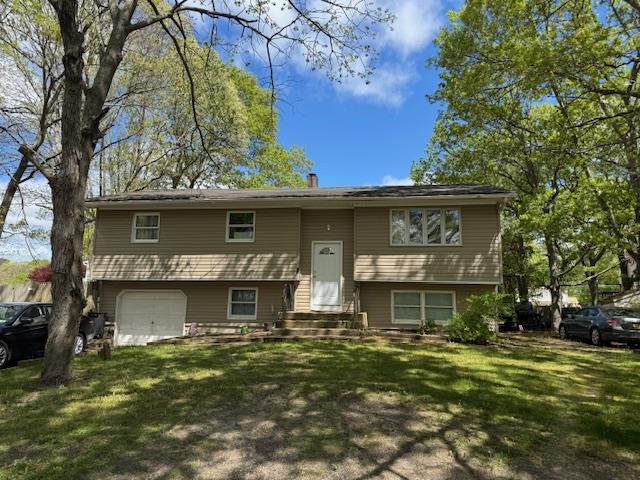 27 Hampton Ave, Mastic, NY 11950 - bi-level home featuring a garage, a front yard, and a chimney