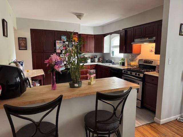 27 Hampton Ave, Mastic, NY 11950 - kitchen with stainless steel range with gas stovetop, wooden counters, a kitchen breakfast bar, under cabinet range hood, and a peninsula