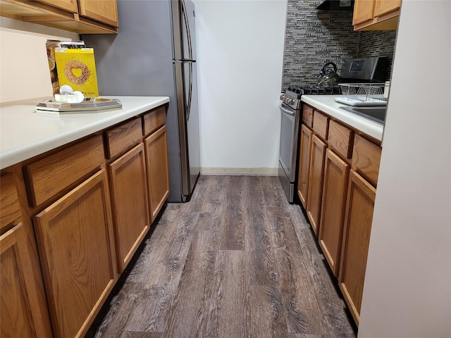 kitchen with light countertops, stainless steel appliances, brown cabinets, decorative backsplash, and dark wood-style floors