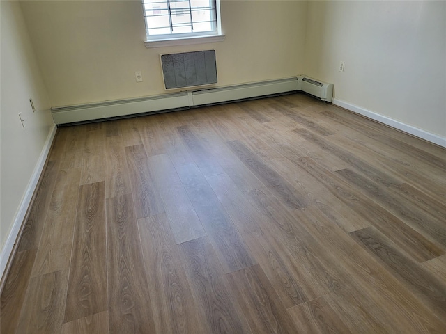 spare room featuring baseboard heating, wood finished floors, and baseboards