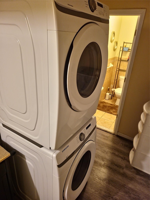 laundry room with laundry area, stacked washer and dryer, dark wood-style flooring, and tile walls