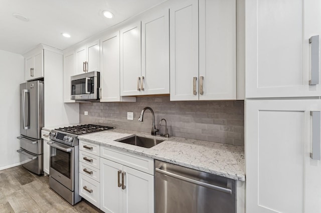kitchen featuring a sink, light wood-style floors, white cabinetry, stainless steel appliances, and backsplash