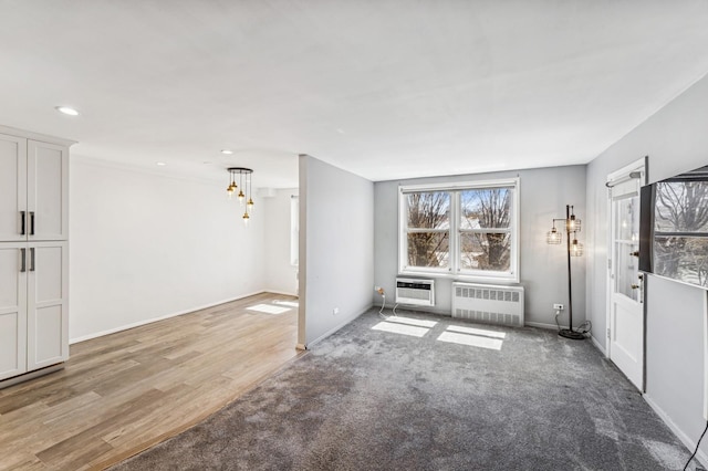 unfurnished living room with baseboards, recessed lighting, radiator heating unit, light carpet, and a wall unit AC