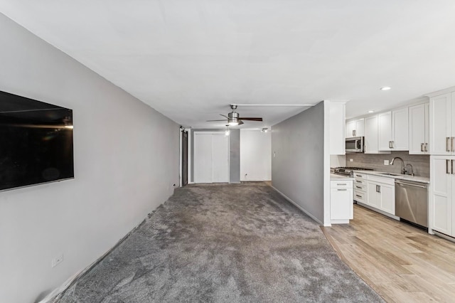 unfurnished living room with baseboards, a sink, ceiling fan, light wood finished floors, and light carpet