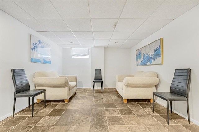 sitting room with baseboards, stone finish flooring, and a paneled ceiling