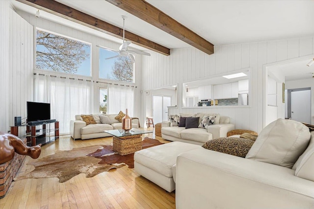 living room featuring wooden walls, beam ceiling, a ceiling fan, a towering ceiling, and hardwood / wood-style flooring