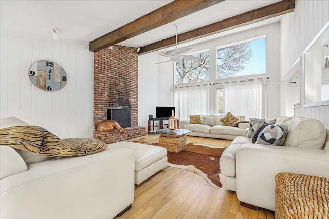 living room featuring wood-type flooring, a fireplace, beamed ceiling, wooden walls, and a ceiling fan