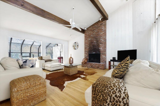 living area with wooden walls, ceiling fan, a brick fireplace, vaulted ceiling with beams, and wood finished floors