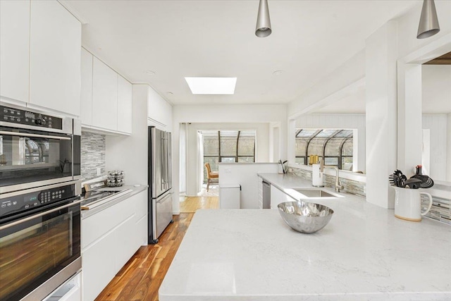 kitchen featuring backsplash, a skylight, appliances with stainless steel finishes, a sink, and white cabinetry
