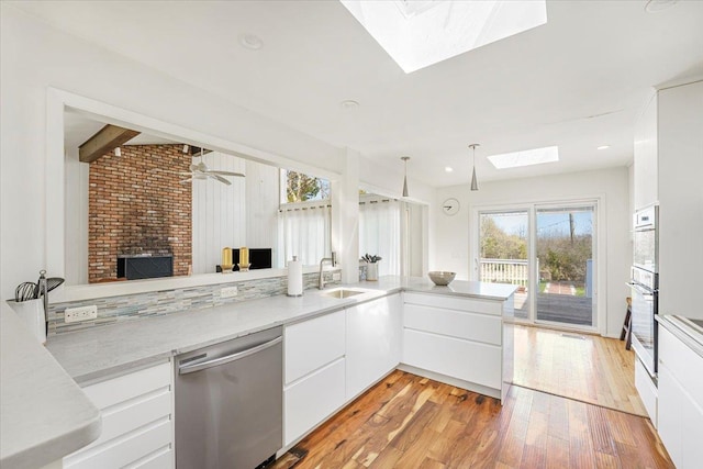 kitchen featuring a sink, light wood finished floors, a fireplace, white cabinetry, and stainless steel dishwasher