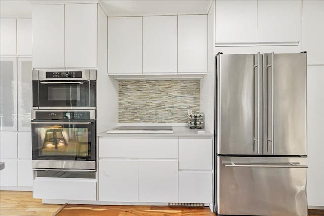 kitchen featuring light wood-type flooring, light countertops, white cabinets, tasteful backsplash, and appliances with stainless steel finishes