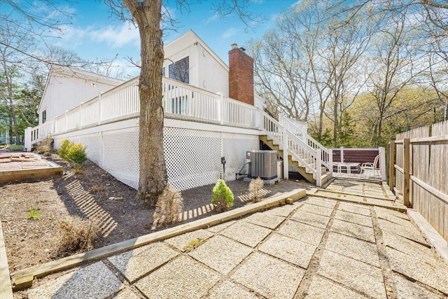 view of side of property with central AC, fence, a deck, a chimney, and stairway