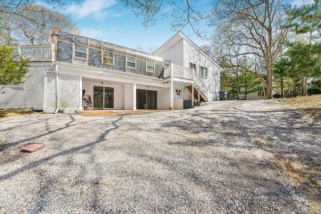 rear view of property with stairs, gravel driveway, a wooden deck, and a chimney