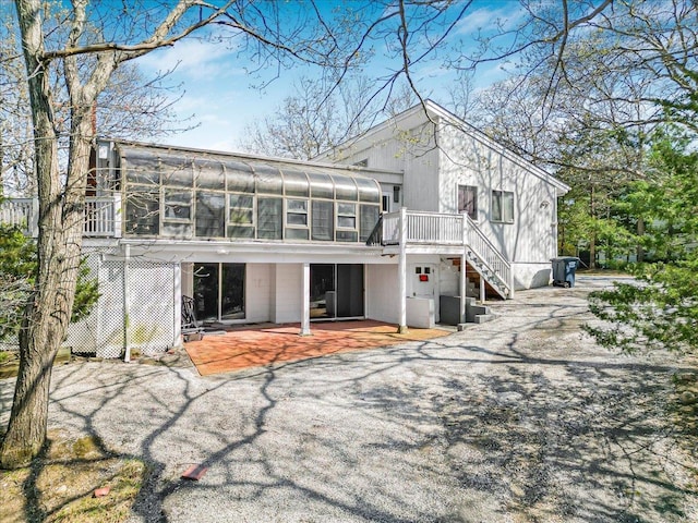 back of property featuring stairway, a wooden deck, a patio area, and a sunroom