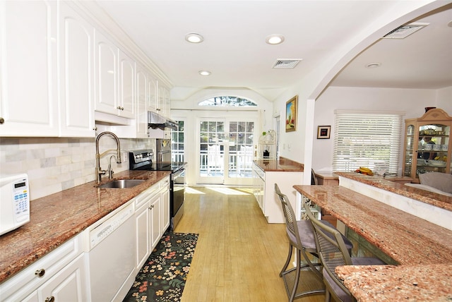 kitchen featuring white appliances, a sink, arched walkways, white cabinets, and stone countertops